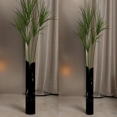 two tall black vases with green plants in them on a table next to a curtain