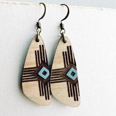 wooden earrings with blue and brown designs hanging from hooks on a white surface next to a piece of fabric