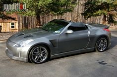 a silver sports car parked in a parking lot next to some trees and fenced in area