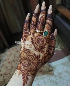 a woman's hand painted with henna and an emerald ring on her finger