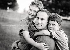 a black and white photo of two boys hugging their father's shoulders in the park