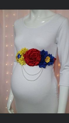 a pregnant woman wearing a white shirt with flowers on it's belt and pearls around the waist