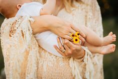 a woman holding a baby with a yellow flower in her lap and wearing a ring