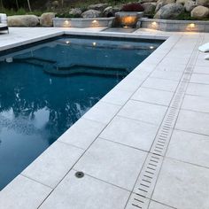 an empty swimming pool surrounded by rocks and landscaping lights are on the side of the pool