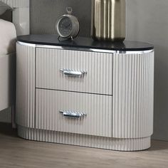 a white nightstand with two drawers and a clock on the top one drawer has a silver vase next to it