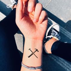 a person with a small tattoo on their wrist holding two crossed swords in one hand