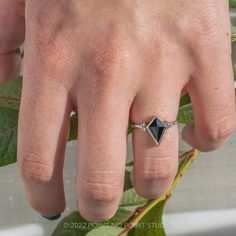 a person's hand with a ring on it and a plant in the background