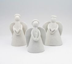 three white ceramic angel figurines sitting next to each other on a white surface