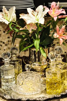 flowers are in vases and glass bottles on a silver platter with other items