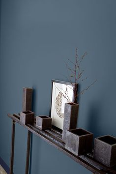 a shelf with vases and candles on it against a blue wall in a living room