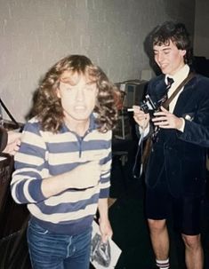 two young men standing next to each other in a room with one holding a camera