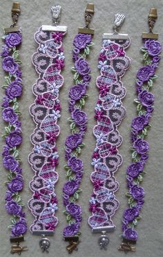 three pieces of purple lace with flowers and beads hanging from hooks on a white surface