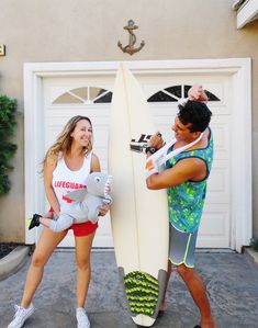 two people dressed up as surfers and one holding a surfboard in front of a garage door