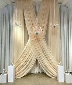 a room with curtains and chandeliers hanging from it's ceiling in front of two white pedestals