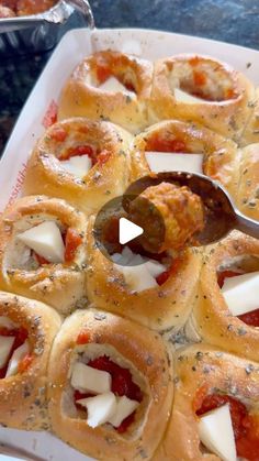 a white tray filled with rolls covered in cheese and tomato sauce next to a serving spoon