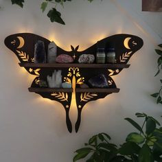 a butterfly shaped wall mounted shelf with candles and rocks on it's sides, next to a potted plant