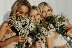 three beautiful young women standing next to each other with flowers in front of their faces