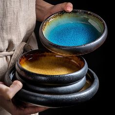 a person is holding three bowls with blue and yellow powder in them on their hands