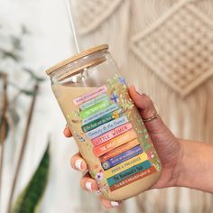 a woman holding a glass jar filled with lots of different colored books and a straw in her hand