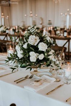 a centerpiece with white flowers and greenery sits on a table at a wedding reception