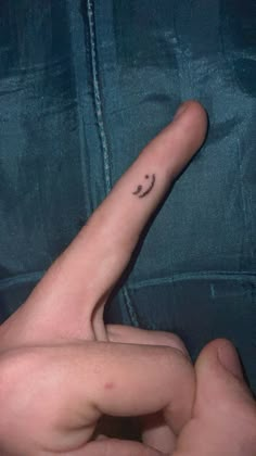 a person's hand with a smiley face tattoo on their left thumb and finger