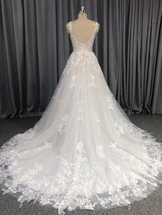 a white wedding dress on display in front of grey curtained backdrop with curtains behind it