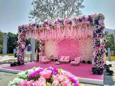 an outdoor wedding setup with pink and white flowers on the stage, surrounded by chairs