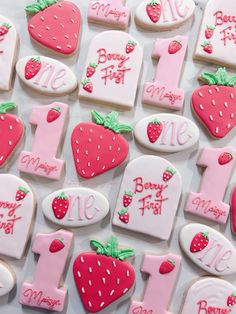 decorated cookies are arranged in the shape of numbers and strawberries for first birthdays