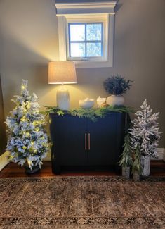 two christmas trees sitting on top of a rug next to a window