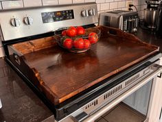 a bowl of tomatoes sitting on top of a wooden cutting board in front of an oven