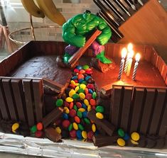 a birthday cake with chocolate and candy in the shape of a hulk figure, surrounded by candles