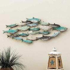 a metal fish wall hanging on the side of a wall next to a potted plant