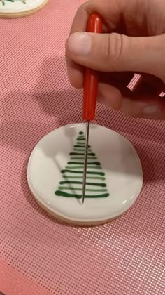 a person is using a needle to cut a christmas tree on a white plate with green and red designs