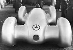 an old black and white photo of a mercedes race car with people standing around it