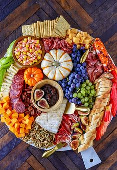 a platter filled with different types of cheeses, crackers and fruit on top of a wooden table