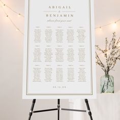 a white table plan sitting on top of a easel next to a vase filled with flowers