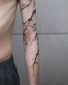 a man's arm covered in black ink with branches and leaves on the arm