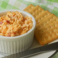 a bowl of dip next to crackers on a plate