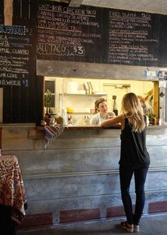 a woman standing in front of a counter at a restaurant with menus on the wall