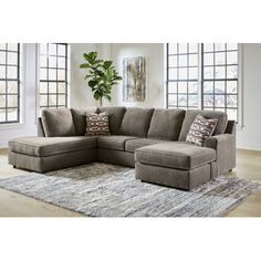 a large sectional couch with pillows on top of it in front of a rug and windows