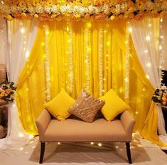 a couch sitting in front of a yellow drape with flowers and lights on it