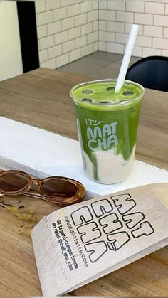 a green smoothie in a plastic cup with a straw and sunglasses on the table