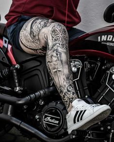 a man with tattoos on his legs sitting on a motorcycle