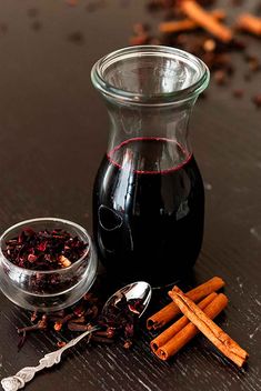 a glass pitcher filled with red wine next to cinnamon sticks and anisette on a table