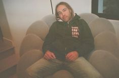 a man sitting in a chair with his legs crossed and looking at the camera while wearing a hoodie