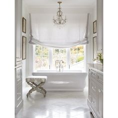 a white bath tub sitting under a window next to a chandelier in a bathroom