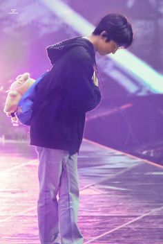 a person standing on a stage with a teddy bear in his hand and lights behind him