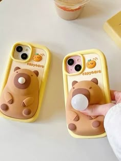 a person is holding two cell phones with bear cases on them, one has a bubble gum in the other's mouth