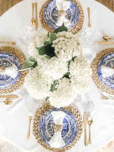 the table is set with blue and white plates, silverware, and hydrangeas