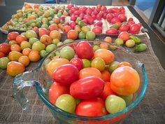 there are many different types of tomatoes in the bowl and on the table, all ready to be picked